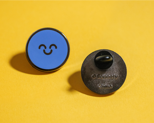 Front and back view of a blue happy face pin on a yellow background