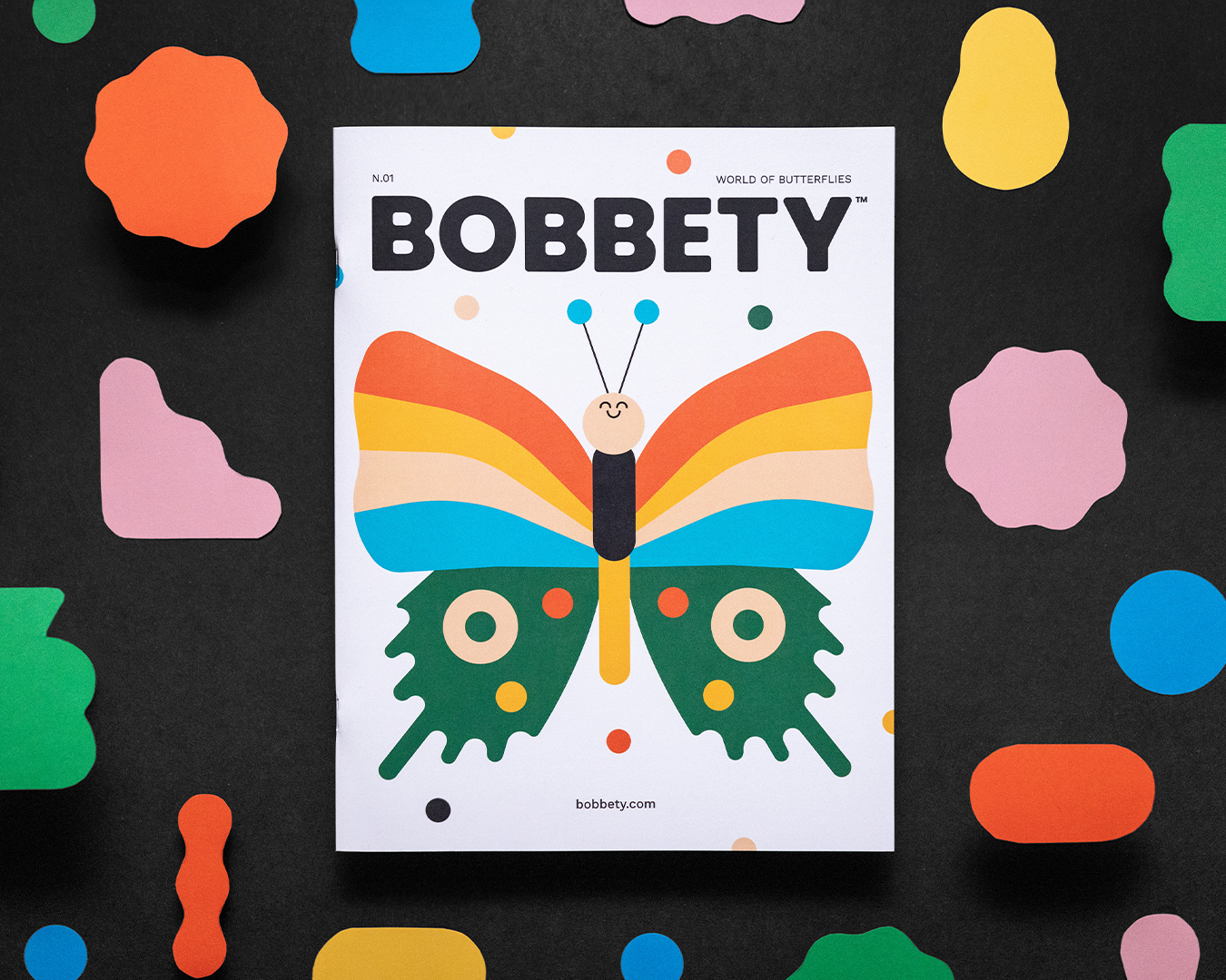 Magazine cover of butterfly and fun cut out shapes on a black background