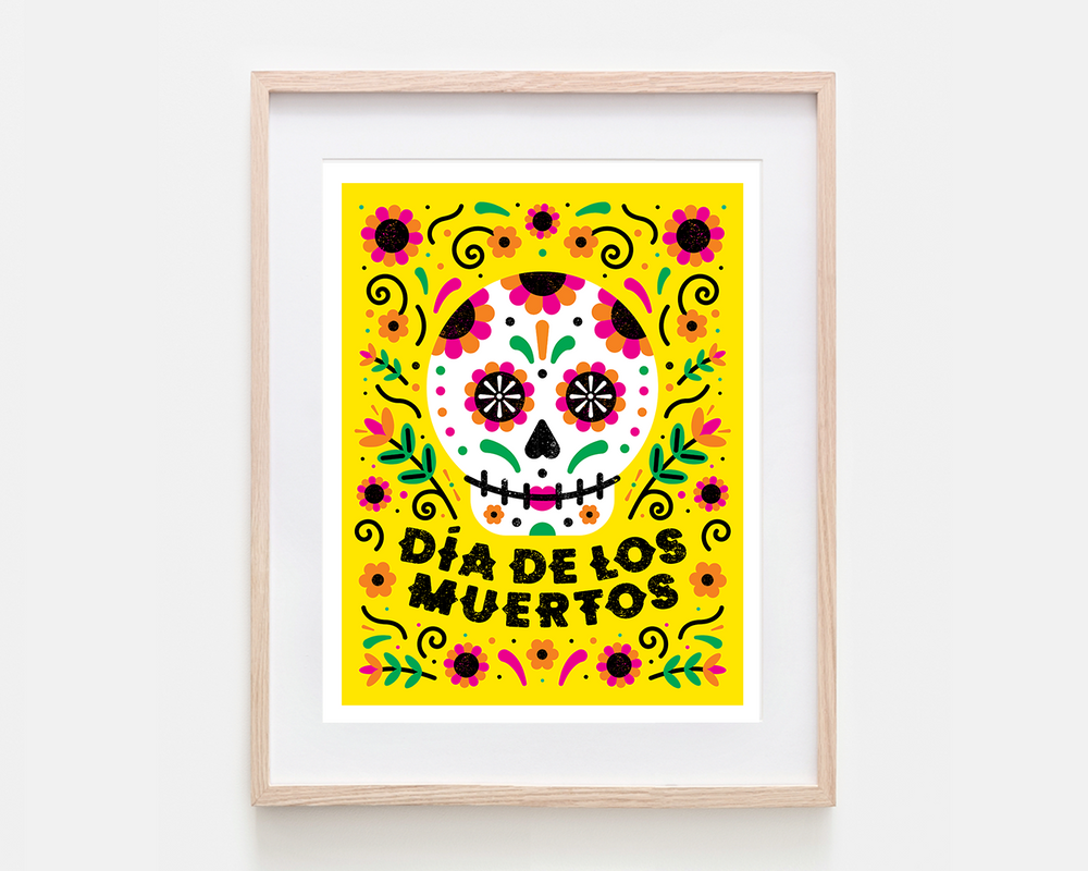 A framed art print featuring a colorful Dia de los Muertos sugar skull design on a bright yellow background, housed in a light natural wood frame with a white mat.