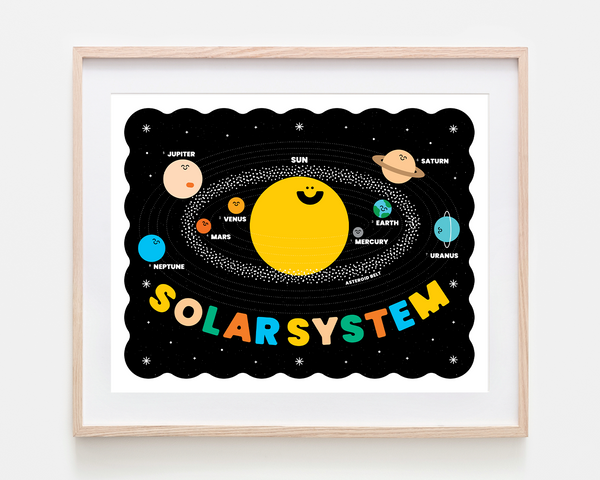 A framed children's educational poster of the Solar System, featuring a cute cartoon sun, planets, and the word 'SOLARSYSTEM' in colorful letters on a black background, housed in a light wood frame.